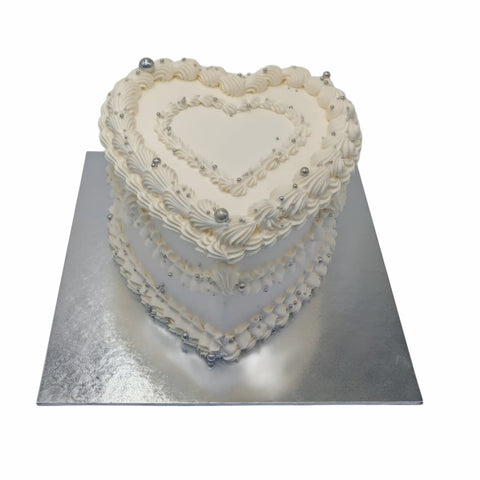 Heart-shaped cake with white frosting and decorative elements on a silver cake stand.